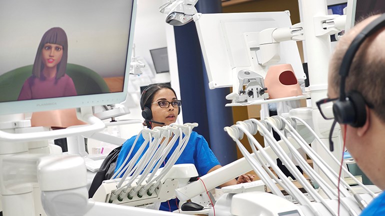 Bild på studenter som kommunikationstränar med virtuella patienter på en digital skärm i klinisk miljö.