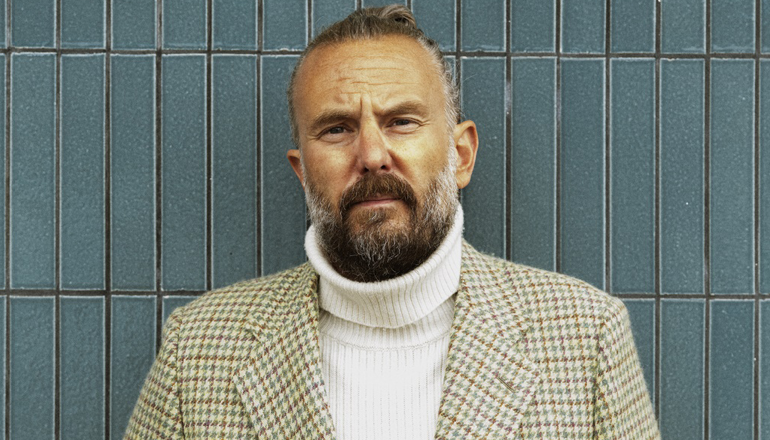 Linus de Faire in a white polo shirt and a checkered blazer.