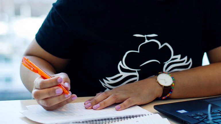 Närbild på student som antecknar framför dator.